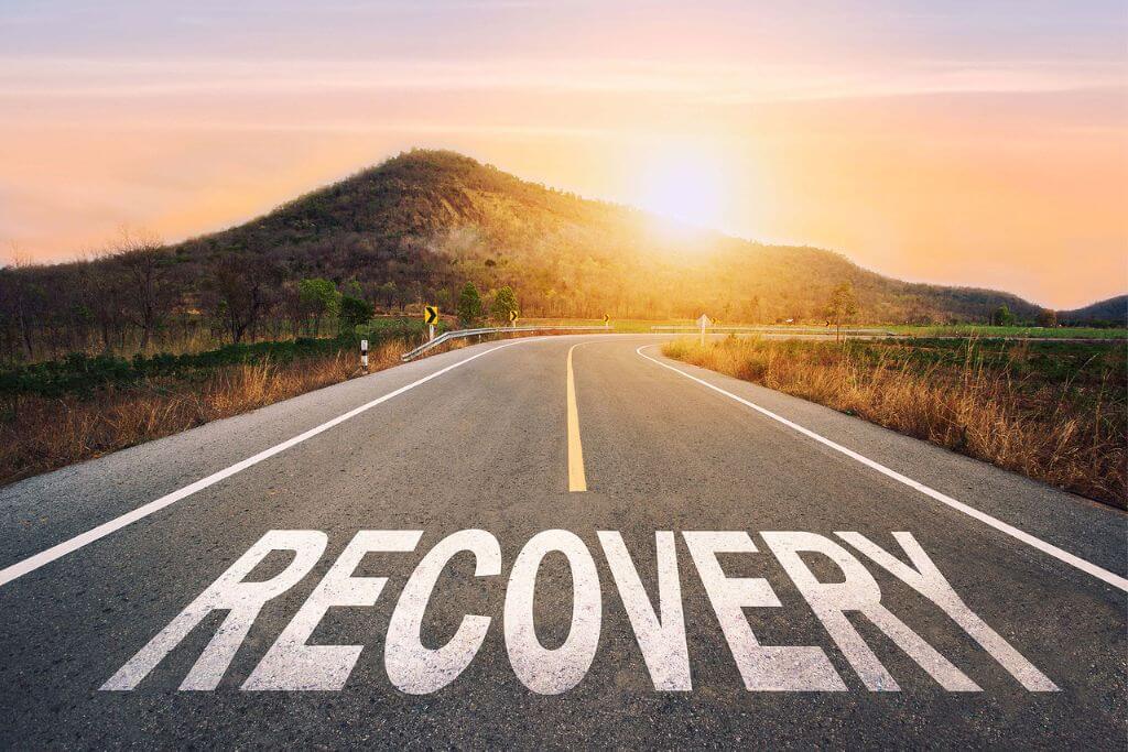 recovery written on highway road in the middle of empty asphalt road of asphalt road at sunset. Road to recovery with sunbream. Concept of coping with the lasting effects of addiction