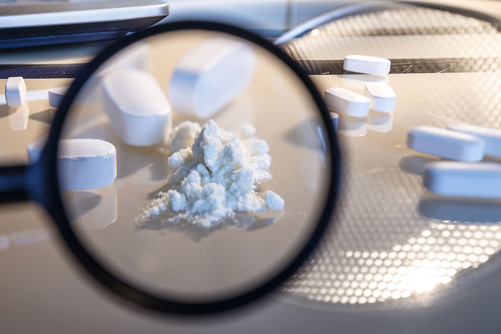 Photo of tablets and a crushed table under a looking glass on the laboratory table as a concept for dangers of buying illicit percocet