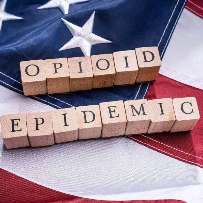 Photo of Opioid Epidemic text on wooden blocks atop American flag. Concept of nitazenes being a growing threat in the opioid crisis.