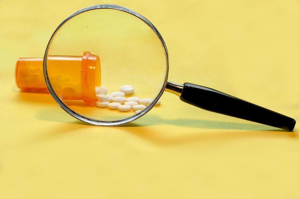 Photo of an open bottle of prescription painkillers with a magnifying glass, concept of buprenorphine vs methadone.