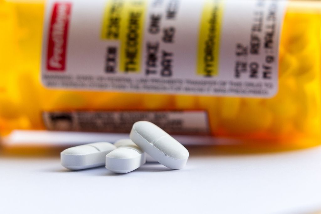 Close-up of white opioid pills in front of a prescription bottle, representing opioid pain medications commonly prescribed for pain management. Concept of hydrocodone vs. oxycodone