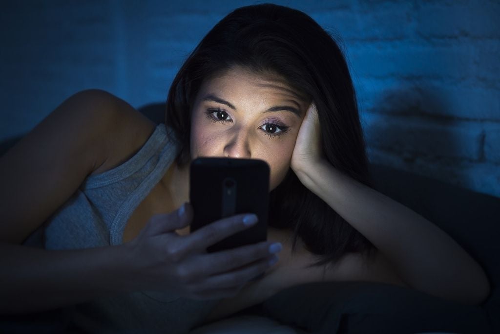 A woman lying in bed looking at a phone, concept of buying prescription drugs on social media