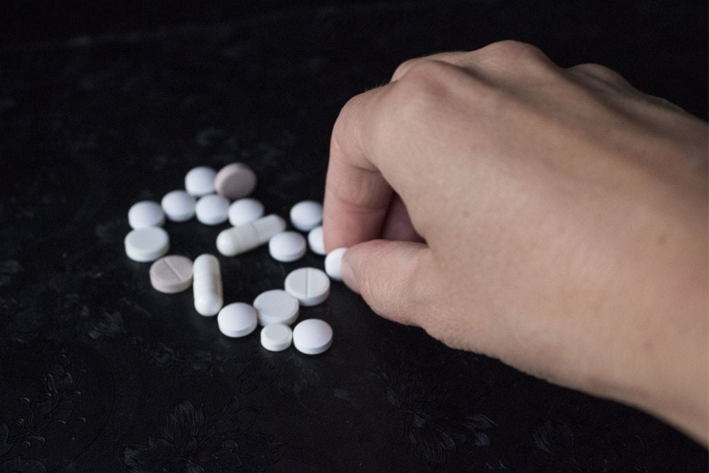 Scattered different pills and capsules close up on a black background with a hand picking up a pill. Concept of polydrug use.